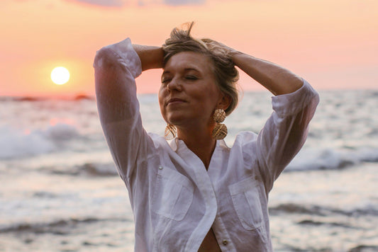 Frau am Meer bei Sonnenuntergang, Hände im Haar, entspannter Ausdruck